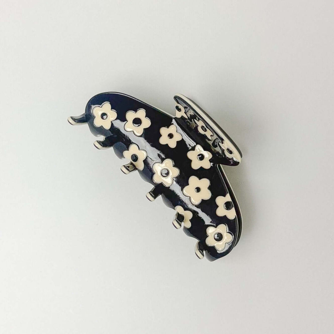 Navy hair clip with white floral designs on a light gray background